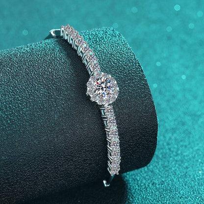 Silver Moissanite Bangle displayed on a textured teal surface, highlighting its sparkling moissanite stones and refined silver craftsmanship.