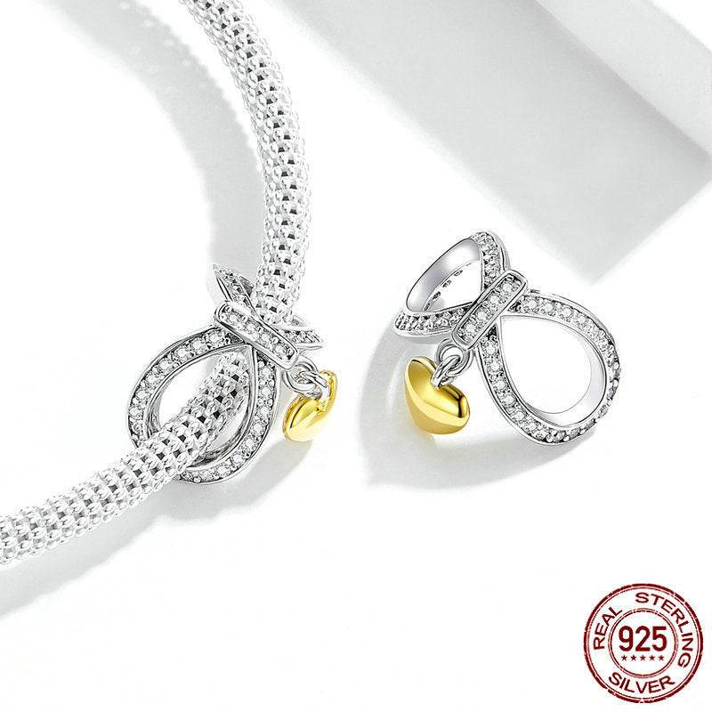 Close-up of a heart infinity charm attached to a sterling silver bracelet, showcasing its crystal details and gold heart pendant.