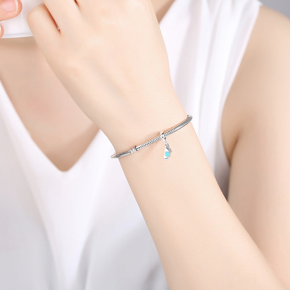 Model wearing a sterling silver bracelet with a baby footprint charm, featuring a turquoise heart. A delicate and sentimental jewelry piece.