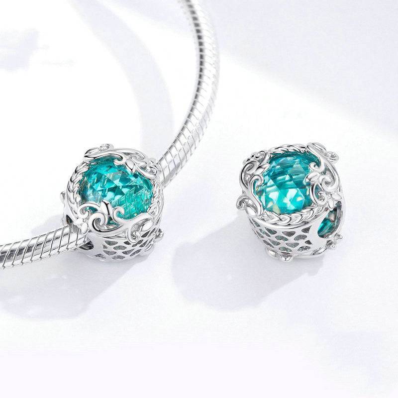 Pair of Aqua Glass Charms displayed on a silver bracelet, showcasing their intricate design and vibrant blue gemstone.