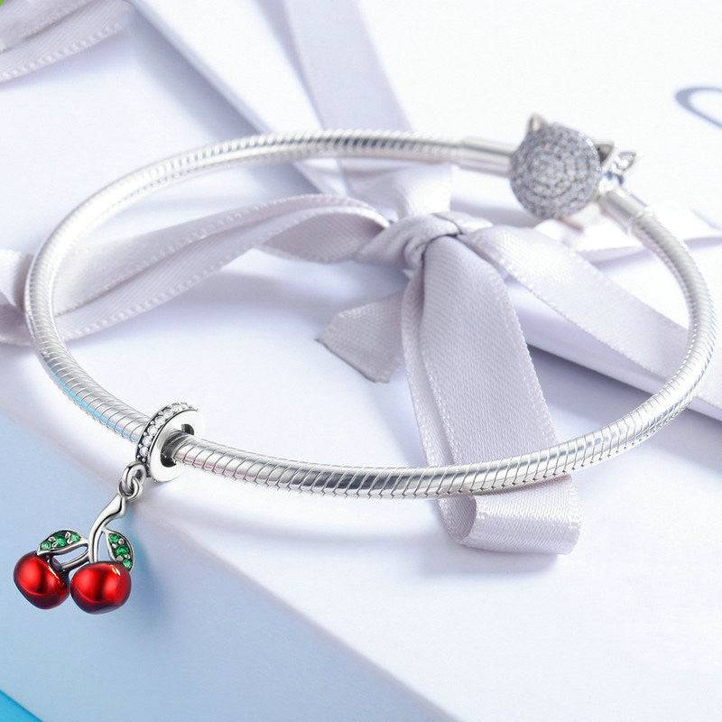 Cherry Charm attached to a silver bracelet, highlighting its vibrant red cherries and green leaf design. A perfect charm for bracelets and necklaces alike.